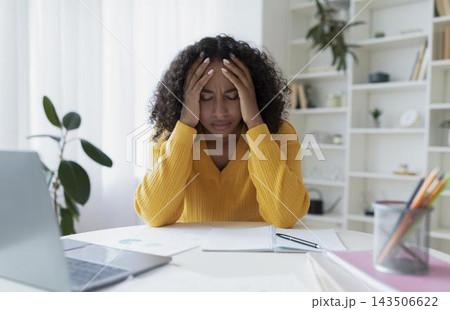 Worried Black Woman In Her 30s Holding Her Head In Stress While Working At Home Office, Feeling Overwhelmed And Stressed Out, Emphasizing Importance Of Mental Health And Self-care. 143506622