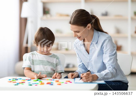 Smiling Caucasian Woman And Young Boy Engaged In Creative Play With Colorful Building Blocks At Home, Sitting At White Table In Cozy Living Room Setting, Enjoying Quality Time Together. 143506637