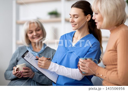 Smiling Female Nurse Engaging With Senior Caucasian Women During Consultation In Modern Healthcare Clinic. Providing Support And Guidance In Comfortable Setting. Healthcare Concept. Smiling Female Nurse Engaging With Senior Caucasian Women During Consultation In Modern Healthcare Clinic. Providing Support And Guidance In Comfortable Setting. Healthcare Concept. 143506956