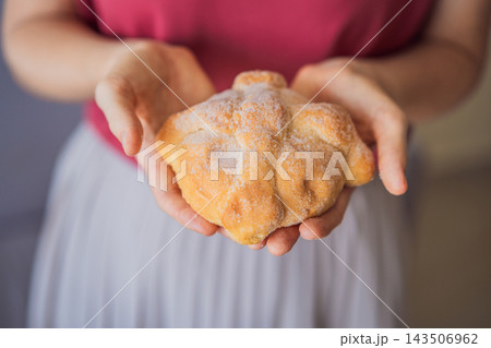 Woman sharing a Mexican Day of the Dead bread with its symbolic bone decoration. Woman sharing a Mexican Day of the Dead bread with its symbolic bone decoration. 143506962