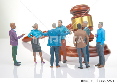 Miniature people engage in discussion near a large gavel figure, reflecting a courtroom scene  143507294