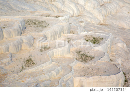 White travertine terraces in Pamukkale, Turkey with small patches of greenery on the slopes White travertine terraces in Pamukkale, Turkey with small patches of greenery on the slopes 143507534