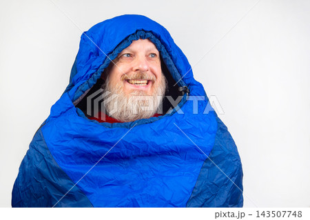 Man smiles while wearing a blue sleeping bag hood in a simple indoor setting Man smiles while wearing a blue sleeping bag hood in a simple indoor setting 143507748