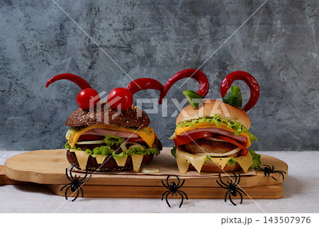 Scary hamburgers with fresh lettuce, tomatoes, cream cheese, lettuce, onions, cutlets and peppers in the form of horns on an old concrete background, cafe advertising, menu, restaurant business card, Scary hamburgers with fresh lettuce, tomatoes, cream cheese, lettuce, onions, cutlets and peppers in the form of horns on an old concrete background, cafe advertising, menu, restaurant business card, 143507976