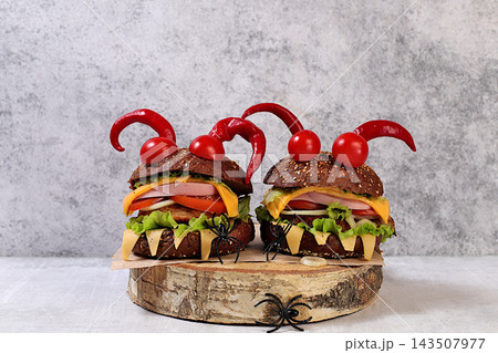 Halloween food concept. Scary hamburgers with fresh lettuce, tomatoes, cream cheese, lettuce, onions, cutlets and peppers in the form of horns on an old concrete background, cafe advertising, menu, 143507977
