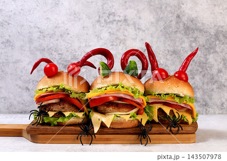 Halloween food concept. Scary hamburgers with fresh lettuce, tomatoes, cream cheese, lettuce, onions, cutlets and peppers in the form of horns on an old concrete background, cafe advertising, menu, Halloween food concept. Scary hamburgers with fresh lettuce, tomatoes, cream cheese, lettuce, onions, cutlets and peppers in the form of horns on an old concrete background, cafe advertising, menu, 143507978