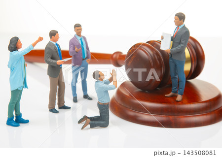 Miniature people interact with a gavel and a figure holding legal documents in a courtroom scene Miniature people interact with a gavel and a figure holding legal documents in a courtroom scene 143508081