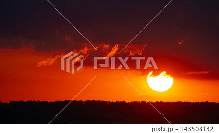 Sunset over the horizon with colorful clouds and a bright sun shining above the trees 143508132