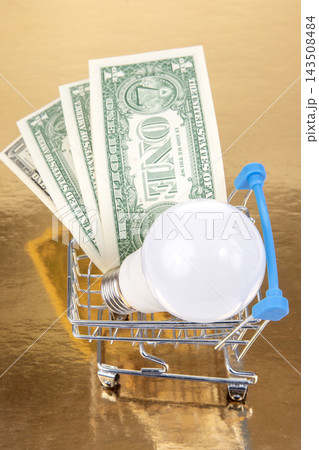 Shopping cart with light bulb and one dollar bills on golden background 143508484