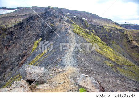 Hiking a path on a rocky mountain in Iceland with green moss and snow on the peaks Hiking a path on a rocky mountain in Iceland with green moss and snow on the peaks 143508547