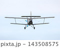 Small plane flies in the sky during daytime near a rural area with fields and trees 143508575