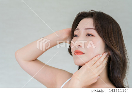 髪とフェイスラインに手を添えて遠くを見つめる30代女性。美しい肌と大人の美容イメージ 143511194