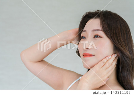 髪と頬に手を添えて優しく微笑む30代女性。美しいフェイスラインと透明感のある肌の美容イメージ 髪と頬に手を添えて優しく微笑む30代女性。美しいフェイスラインと透明感のある肌の美容イメージ 143511195