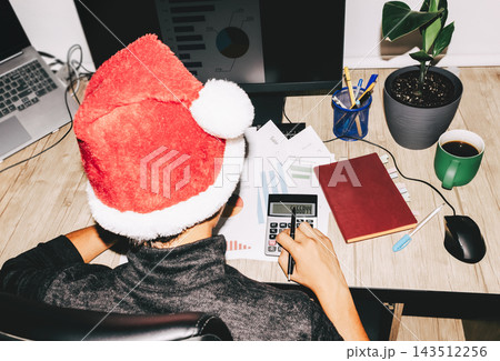 Santa hat worker calculating sales report at office desk Santa hat worker calculating sales report at office desk 143512256