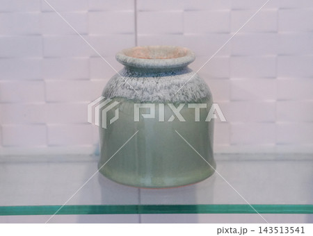 front view antique green and white ceramic pot, on a glass shelf, white ceramic wall background, object, decor, fashion, copy space 143513541