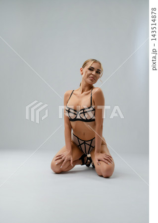 Blonde woman in geometric mesh lingerie kneeling in studio 143514878