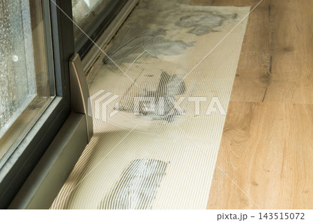 On a clean vinyl floor, sticky adhesive marks are being meticulously removed near a bright glass sliding door, showing the maintenance of interior surfaces. On a clean vinyl floor, sticky adhesive marks are being meticulously removed near a bright glass sliding door, showing the maintenance of interior surfaces. 143515072