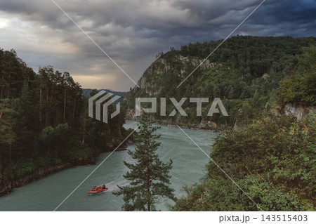Motorboat sailing on Katun River through mountain valley under dramatic sky Motorboat sailing on Katun River through mountain valley under dramatic sky 143515403