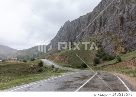 Winding asphalt road through scenic mountain ridge under cloudy overcast sky Winding asphalt road through scenic mountain ridge under cloudy overcast sky 143515575