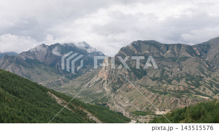 Panoramic mountain range with rocky cliffs and green valleys under cloudy sky 143515576