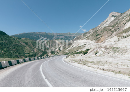 Winding asphalt mountain road curve through scenic rocky valley under clear blue sky Winding asphalt mountain road curve through scenic rocky valley under clear blue sky 143515667