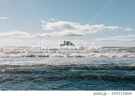 Ocean waves crashing near sea stack rock formation under cloudy blue sky Ocean waves crashing near sea stack rock formation under cloudy blue sky 143515804