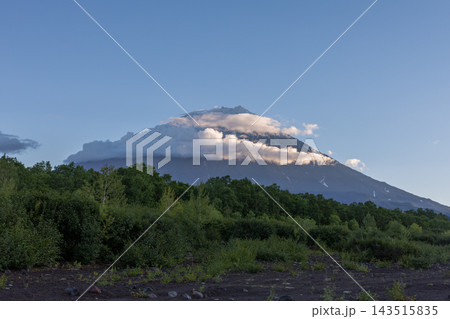 Majestic volcanic peak enveloped in evening clouds above green forest Majestic volcanic peak enveloped in evening clouds above green forest 143515835