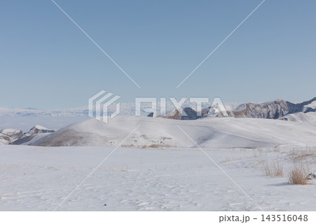 Snow covered rolling hills and mountain ridges under clear blue sky 143516048