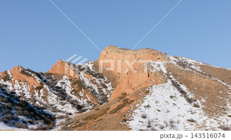 Red sandstone mountain cliffs and snowy slopes of Jeti Oguz gorge under clear blue sky Red sandstone mountain cliffs and snowy slopes of Jeti Oguz gorge under clear blue sky 143516074