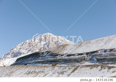 Snow-covered mountain pass road with distant transport trucks in winter Snow-covered mountain pass road with distant transport trucks in winter 143516196