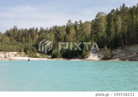 Person paddleboarding on a vibrant azure kaolin quarry lake by Kyshtym pine woods Person paddleboarding on a vibrant azure kaolin quarry lake by Kyshtym pine woods 143516251