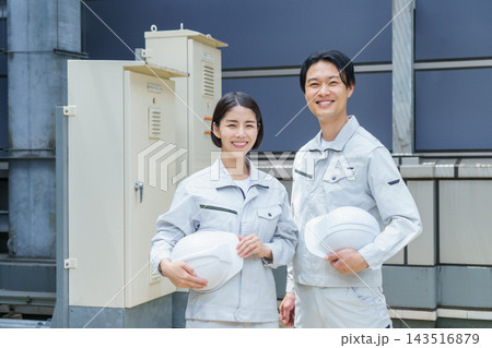 ヘルメットを持って屋上の消化用補給級水槽の前に立つ若い日本人の男女2人のポートレート ヘルメットを持って屋上の消化用補給級水槽の前に立つ若い日本人の男女2人のポートレート 143516879