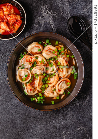 Dumplings served in a bowl with broth and green onions. 143518991