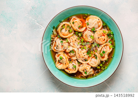 Dumplings served in a bowl with broth and green onions. 143518992