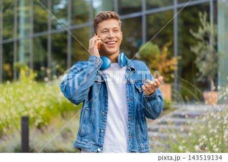 Young man talking on phone during call walking in city street with friendly relaxed smile outdoors 143519134