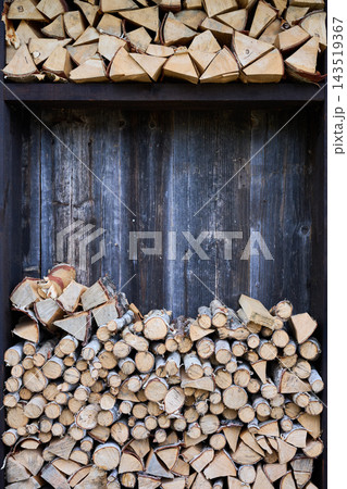 Chopped firewood stored in wooden rack against rustic wall. Stacked logs arranged in sections 143519367
