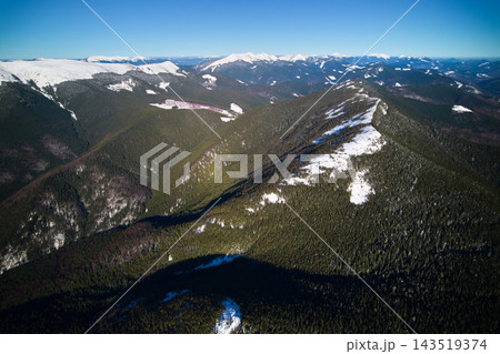 Aerial view of snow covered mountain ridges and evergreen forest under clear blue sky 143519374