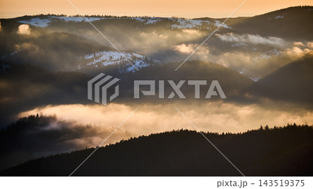 Sunlit cloud inversion drifting through mountain valleys with shadowed ridges and winter traces 143519375