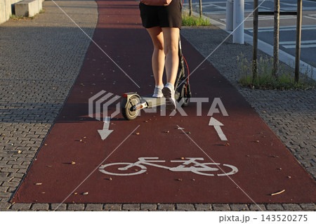 Electric scooter traveling along a dedicated cycling path marked with bicycle symbols and directional arrows, urban micromobility, road safety, shared routes, and modern city infrastructure. 143520275