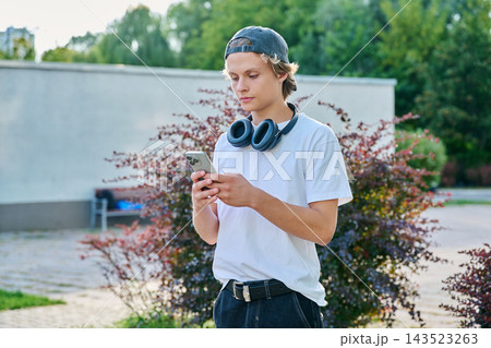 Teenage boy with headphones using smartphone outdoors in summer park 143523263