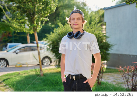 Confident teenage boy with headphones around neck posing outdoors in summer park Confident teenage boy with headphones around neck posing outdoors in summer park 143523265