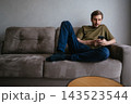 Man relaxing on a comfortable sofa, leaning back against the cushions and interacting with his mobile phone, browsing online content or sending messages in a casual setting 143523544