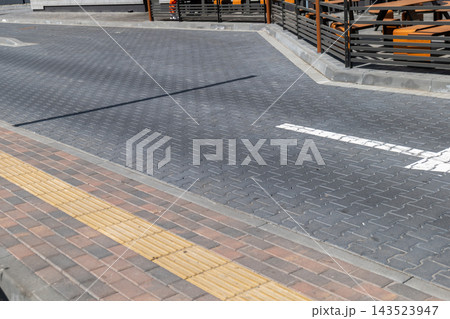 A road intersection shows a textured pavement and a clear pedestrian path. The setting is in an urban area with nearby structures 143523947