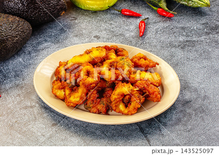 Golden fried squid rings served on beige plate with avocado and red chili peppers in background as seafood appetizer Golden fried squid rings served on beige plate with avocado and red chili peppers in background as seafood appetizer 143525097