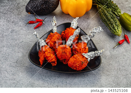Fried chicken lollipop platter with crispy breaded wings on black triangular plate accompanied by fresh bell pepper and chili appetizer 143525108