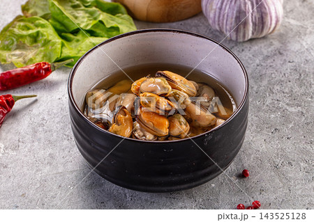 Grey stone surface black ceramic bowl containing cooked orange mussels in clear broth seafood appetizer Grey stone surface black ceramic bowl containing cooked orange mussels in clear broth seafood appetizer 143525128