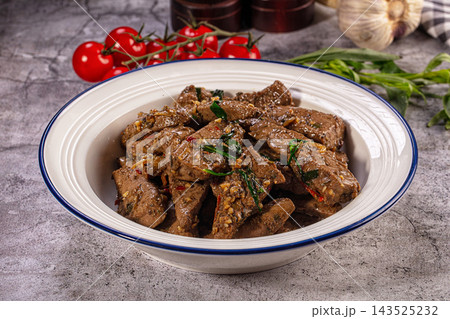 White enamel bowl with blue rim filled with fried beef liver slices garnished with holy basil and chili pepper on gray stone table White enamel bowl with blue rim filled with fried beef liver slices garnished with holy basil and chili pepper on gray stone table 143525232