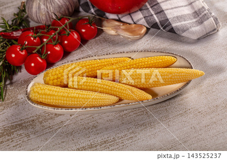 Baby corn cobs on ceramic plate with cherry tomatoes garlic and rosemary in rustic kitchen setting food preparation Baby corn cobs on ceramic plate with cherry tomatoes garlic and rosemary in rustic kitchen setting food preparation 143525237