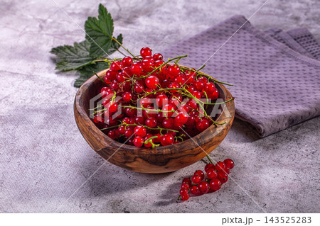 Red currant berries piled inside wooden bowl beside green leaf on textured grey countertop surface, fresh summer fruit harvest Red currant berries piled inside wooden bowl beside green leaf on textured grey countertop surface, fresh summer fruit harvest 143525283