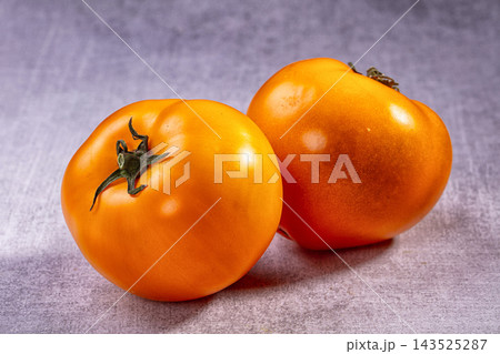 Fresh orange tomatoes with green stems resting on textured gray surface, produce Fresh orange tomatoes with green stems resting on textured gray surface, produce 143525287